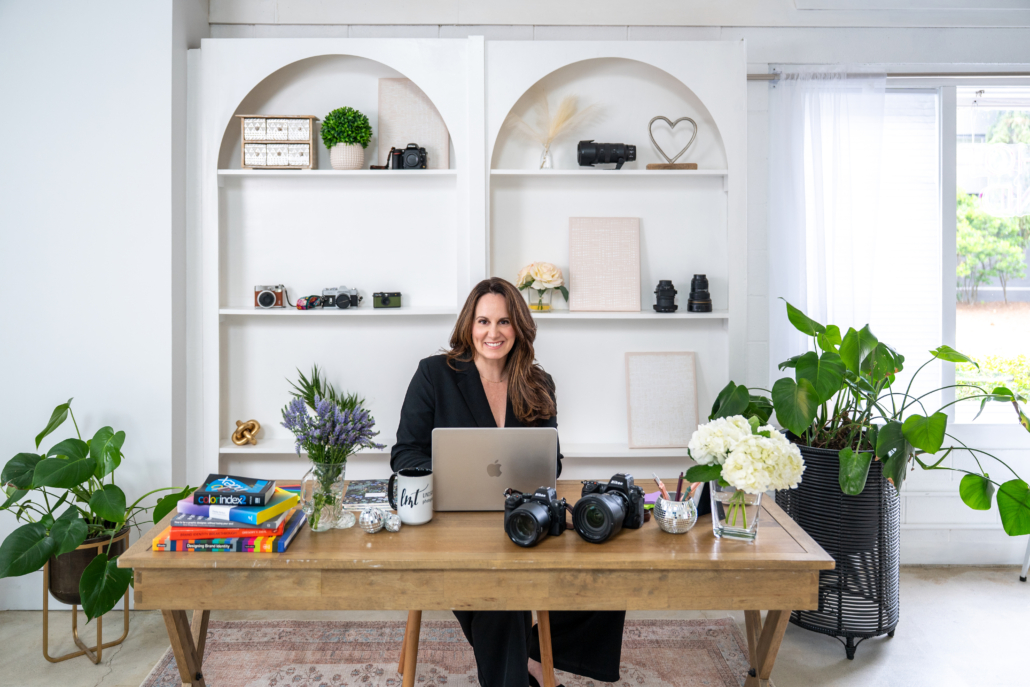 Lindsay Tiwald is a Northern New Jersey Brand Photographer and Interior Photographer. In this photo she sits behind a desk with cameras and photography gear.