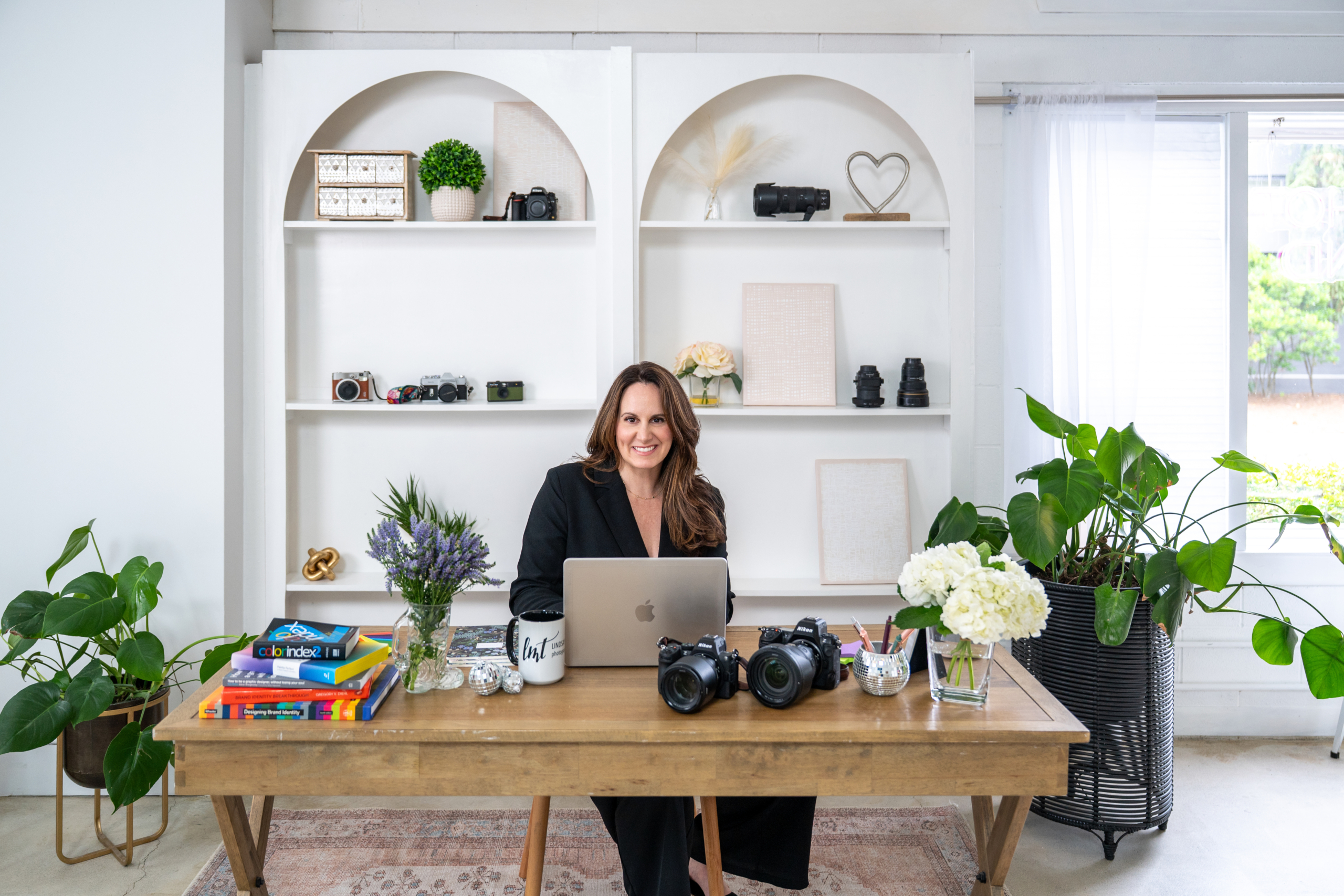 Lindsay Tiwald is a Northern New Jersey Brand Photographer and Interior Photographer. In this photo she sits behind a desk with cameras and photography gear.